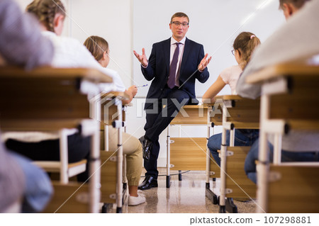 Friendly male teacher working with teen students in classroom Friendly male teacher working with teen students in classroom 107298881