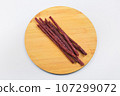 Delicious dried red meat sausages. Thin sausages on a wooden board on a white background. 107299072