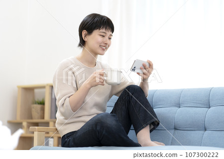 Young woman sitting on sofa and using smartphone 107300222