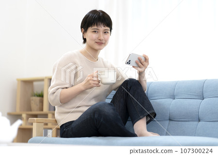 Young woman sitting on sofa and using smartphone Young woman sitting on sofa and using smartphone 107300224