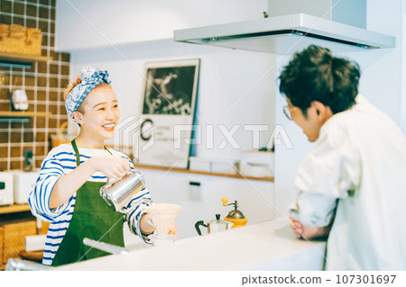 A woman making coffee in the kitchen and a man watching over her A woman making coffee in the kitchen and a man watching over her 107301697