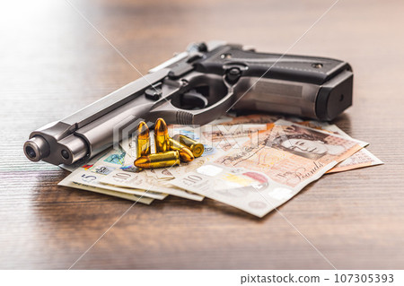 Handgun, bullets and  british pound sterling on wooden table. 107305393