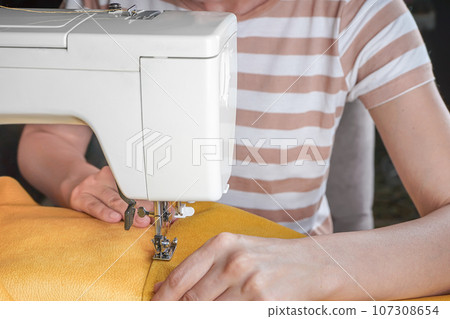 Tailor hands stitching yellow fabric on modern sewing machine at workplace in atelier 107308654