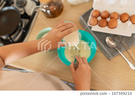 the cooking process, the woman adds milk to the pancake batter the cooking process, the woman adds milk to the pancake batter 107309210