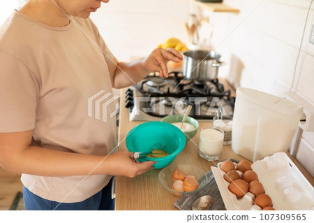 a housewife makes pancakes and kneads the dough while standing at the work surface 107309565