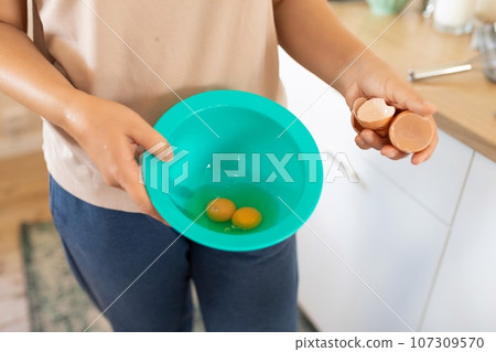 a woman breaks chicken eggs in a bowl while standing in the kitchen a woman breaks chicken eggs in a bowl while standing in the kitchen 107309570