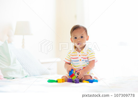 Baby boy playing on bed in sunny nursery Baby boy playing on bed in sunny nursery 107309778