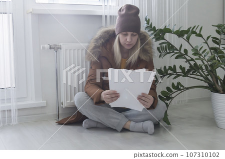 A woman warmly dressed in a brown jacket and hat is sitting near the heater 107310102