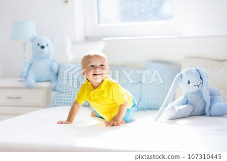 Baby boy playing on bed in sunny nursery Baby boy playing on bed in sunny nursery 107310445