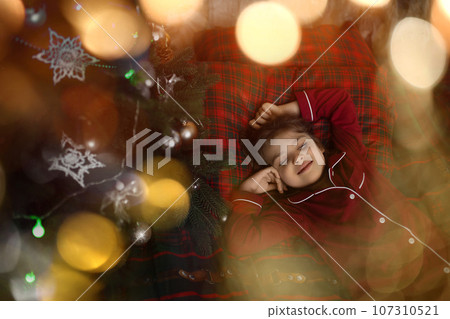 6 years old girl in red pajamas sleeping in bed in holiday lights 107310521