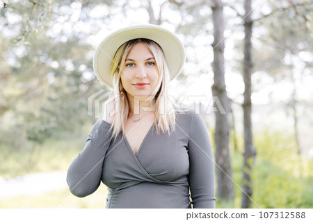 Beautiful pregnant woman in hat and dress walking in the forest. Woman expecting baby born. Beautiful pregnant woman in hat and dress walking in the forest. Woman expecting baby born. 107312588