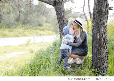 Pregnant woman with kid outdoors. Mother and her son on nature in spring forest. Little child boy kissing mother, who pregnant for second time. Pregnant woman with kid outdoors. Mother and her son on nature in spring forest. Little child boy kissing mother, who pregnant for second time. 107312589