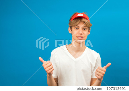 Pleased seller smiling to camera and gesturing thumbs up, approval hand sign, satisfied with result. Indoor studio shot isolated on blue background Pleased seller smiling to camera and gesturing thumbs up, approval hand sign, satisfied with result. Indoor studio shot isolated on blue background 107312691