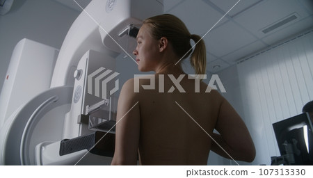 Woman stands topless undergoing mammography screening checkup 107313330