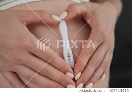 Caucasian woman holding a positive express pregnancy test against the background of her tummy.  107313415