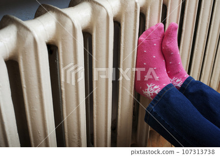 Female warming up her feet on central heating radiator 107313738