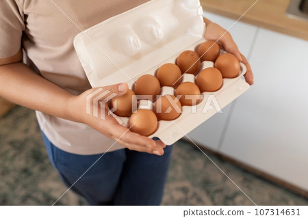 A woman holds chicken eggs in her hands while standing in the kitchen 107314631