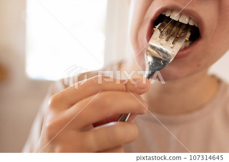 a woman has breakfast with pancakes in her kitchen. close-up of putting food in mouth 107314645