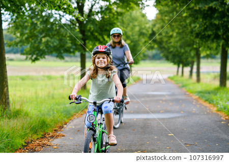 Happy family is riding bikes outdoors and smiling. Mother and daughter, cute little preeschool girl on bicycles, active leisure and sports together. 107316997