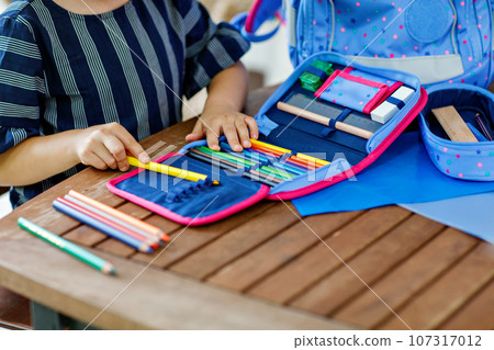 Happy smiling girl preparing for school her backpack. First day of school. Back to school concept. Little child collecting different supplies like pens and books in a bag or satchel. Happy smiling girl preparing for school her backpack. First day of school. Back to school concept. Little child collecting different supplies like pens and books in a bag or satchel. 107317012