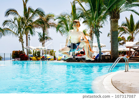 Happy little kid boy jumping in the pool and having fun on family vacations in a hotel resort. Healthy child playing in water. Happy little kid boy jumping in the pool and having fun on family vacations in a hotel resort. Healthy child playing in water. 107317087