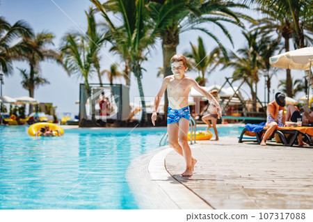 Happy little kid boy jumping in the pool and having fun on family vacations in a hotel resort. Healthy child playing in water. Happy little kid boy jumping in the pool and having fun on family vacations in a hotel resort. Healthy child playing in water. 107317088