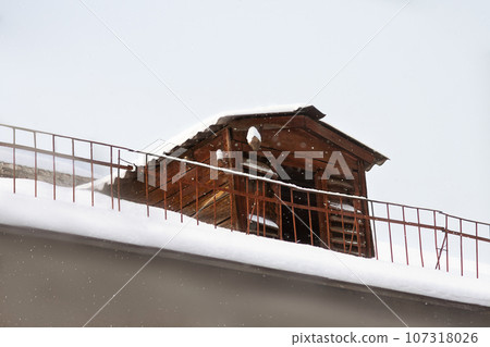 Wooden dovecote or bird house on roof of house with fence. Snowing, winter. Copy space Wooden dovecote or bird house on roof of house with fence. Snowing, winter. Copy space 107318026