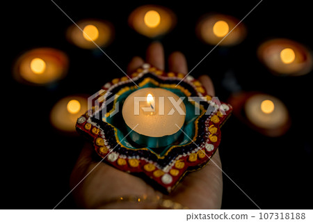 Happy Diwali - Woman hands with henna holding lit candle isolated on dark background. 107318188
