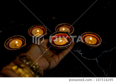 Happy Diwali - Woman hands with henna holding lit candle isolated on dark background. Happy Diwali - Woman hands with henna holding lit candle isolated on dark background. 107318295