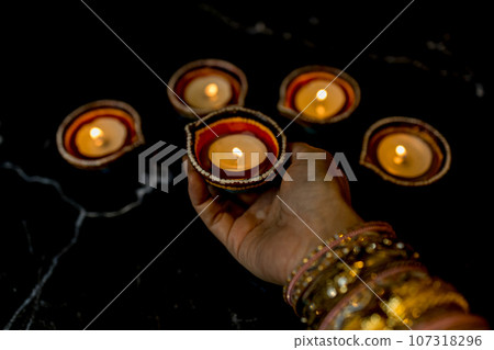 Happy Diwali - Woman hands with henna holding lit candle isolated on dark background. 107318296