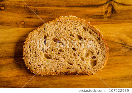 one cut piece of rye bread lies on a wooden plank. 107322989
