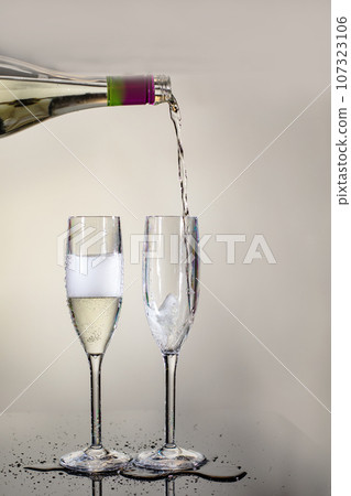 champagne is poured from a bottle into glasses. two glasses 107323106