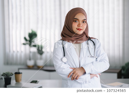 Portrait of a confident Asian Muslim female doctor with her arms crossed, wearing a brown hijab. 107324565