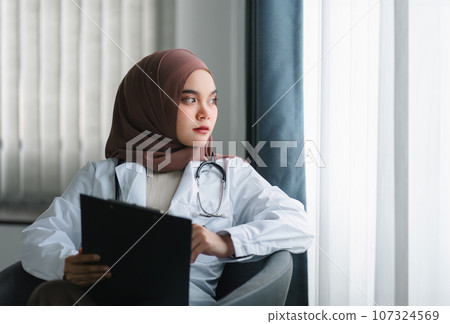 smiling muslim female doctor in brown hijab carrying medical records. 107324569