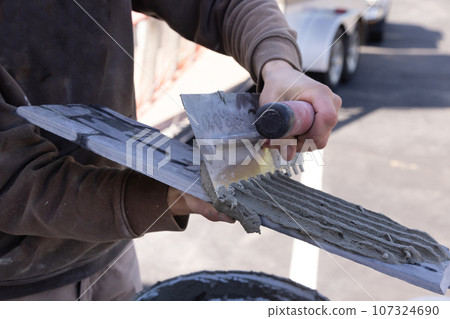 Before applying tiles man spreads wet cement adhesive with trowels 107324690