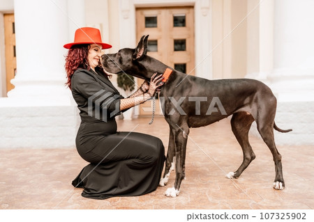 A photo of a woman and her Great Dane walking through a town, taking in the sights and sounds of the urban environment. 107325902