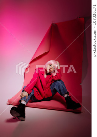 Woman model sitting on pink background at photo shoot in studio. Woman model sitting on pink background at photo shoot in studio. 107326171