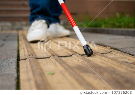A blind woman walks on the street on tactile yellow tiles. Focus on the tactile cane.  107326208