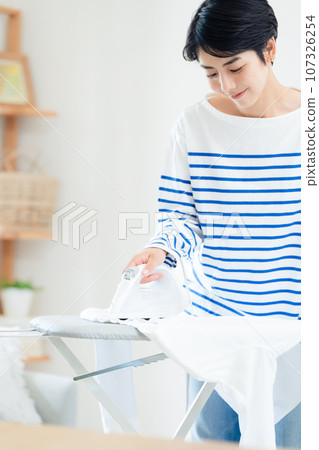 Smiling woman ironing clothes in the living room 107326254