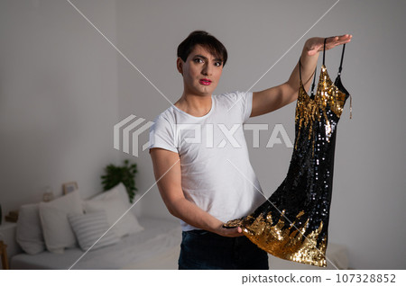 Gay trying on a shiny dress. The transgender chooses the outfit for the party. Gay trying on a shiny dress. The transgender chooses the outfit for the party. 107328852