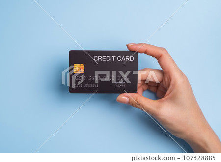 Top view of hand holding black credit card on blue background. 107328885