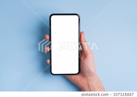 Top view of hand holding black smartphone with blank screen on blue background. 107328887
