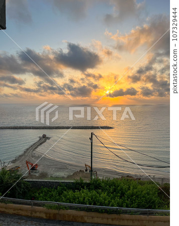 An excavator makes a mound of sand on the seashore. Protection of the beach area for the winter from flooding. Industrial construction equipment and machinery. 107329444