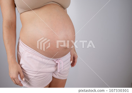 Close-up of pregnant woman's belly in third trimester on white background. Copy space.  107330301