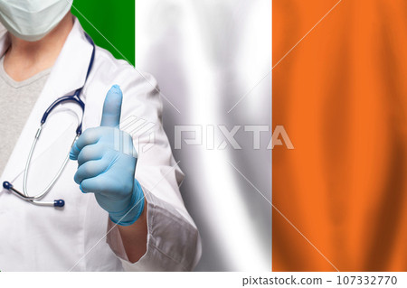 Irish doctor's hand showing thumb up positive gesture on flag of Ireland background Irish doctor's hand showing thumb up positive gesture on flag of Ireland background 107332770