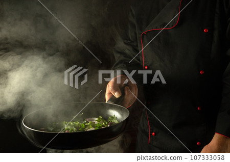 Molecular gastronomy or cuisine. The cook prepares fresh vegetables in a frying pan. Restaurant or hotel menu with advertising space on black background 107333058