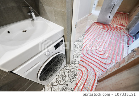 Comparison of washroom lavatory before and after renovation. Old apartment restroom with underfloor heating pipes and new renovated room with washbasin and washing machine. Comparison of washroom lavatory before and after renovation. Old apartment restroom with underfloor heating pipes and new renovated room with washbasin and washing machine. 107333151