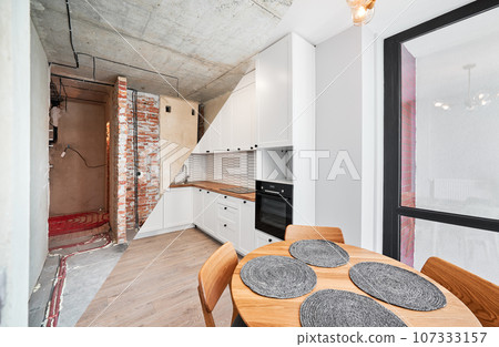 Modern apartment before and after restoration or refurbishment. Comparison of old kitchen room and new place with parquet floor, table, kitchen counter, stove and white walls. Home renovation concept. Modern apartment before and after restoration or refurbishment. Comparison of old kitchen room and new place with parquet floor, table, kitchen counter, stove and white walls. Home renovation concept. 107333157