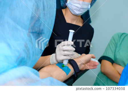 Injecting anesthesia through a catheter on a man's arm on the operating table. Injecting anesthesia through a catheter on a man's arm on the operating table. 107334038