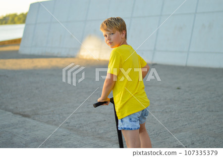 Child on a scooter in the park. A little boy rides a scooter on a sunny day. Active sports for preschoolers 107335379